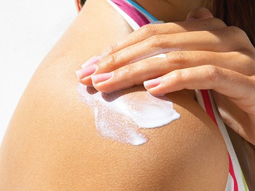 Image of a woman applying sunscreen or suntan lotion on her shoulder.